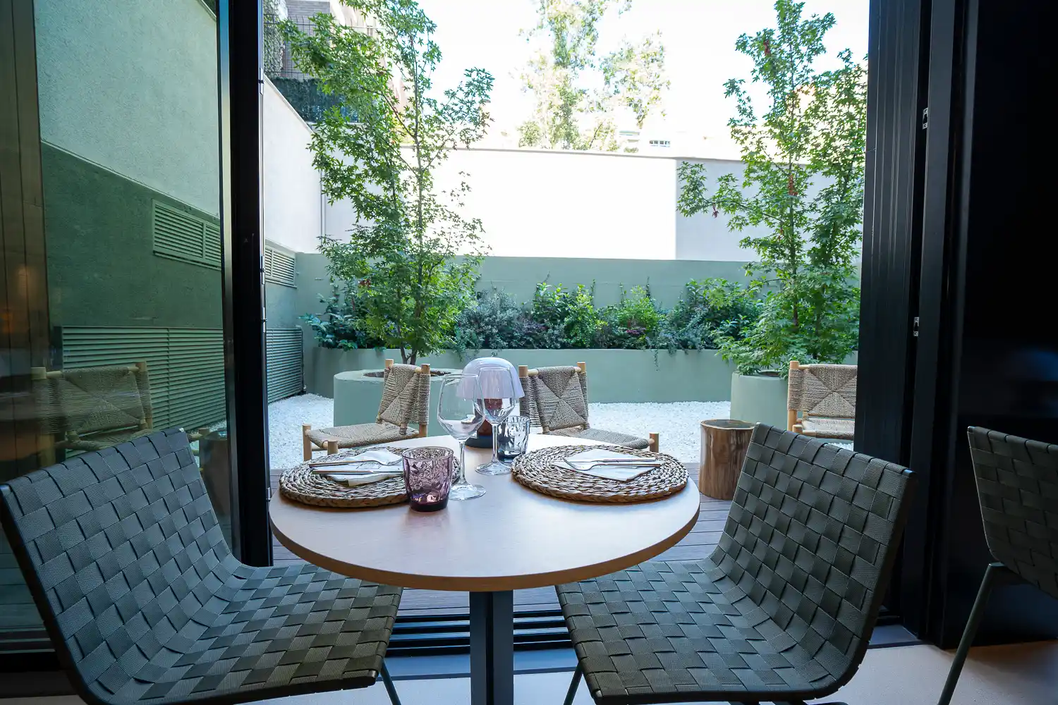 Mesa puesta junto a la cristalera del comedor de Marés, abierta al patio interior con árboles