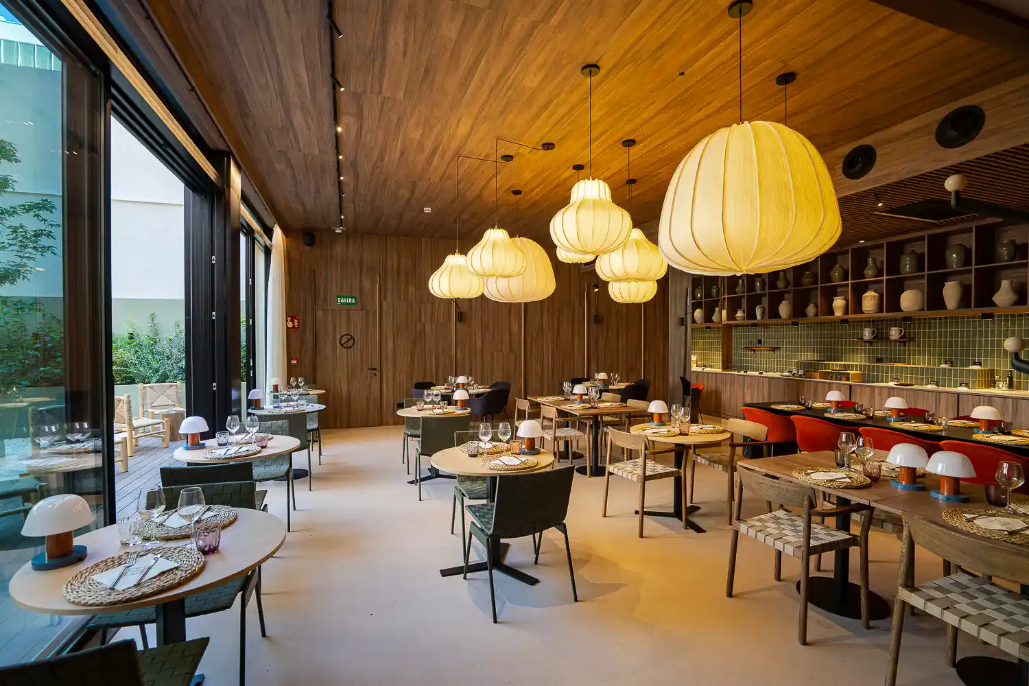 Comedor de Marés con techo de madera, lámparas de papel y ventanales que dan al patio